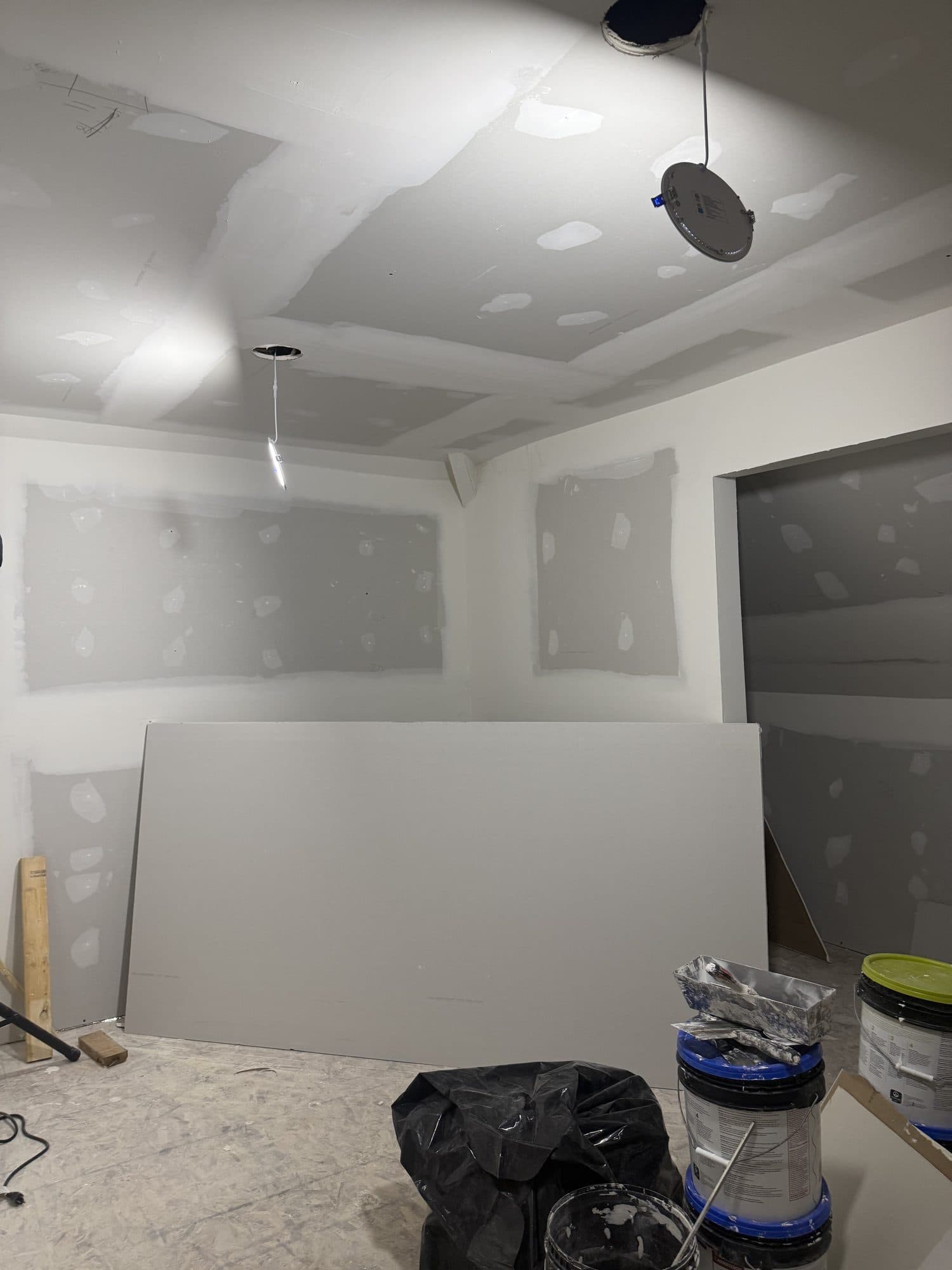 A basement remodel with freshly hung and mudded drywall, recessed-light cutouts, and finishing materials staged. Home addition project by Potts Brothers Construction, Arlington & Northern Virginia