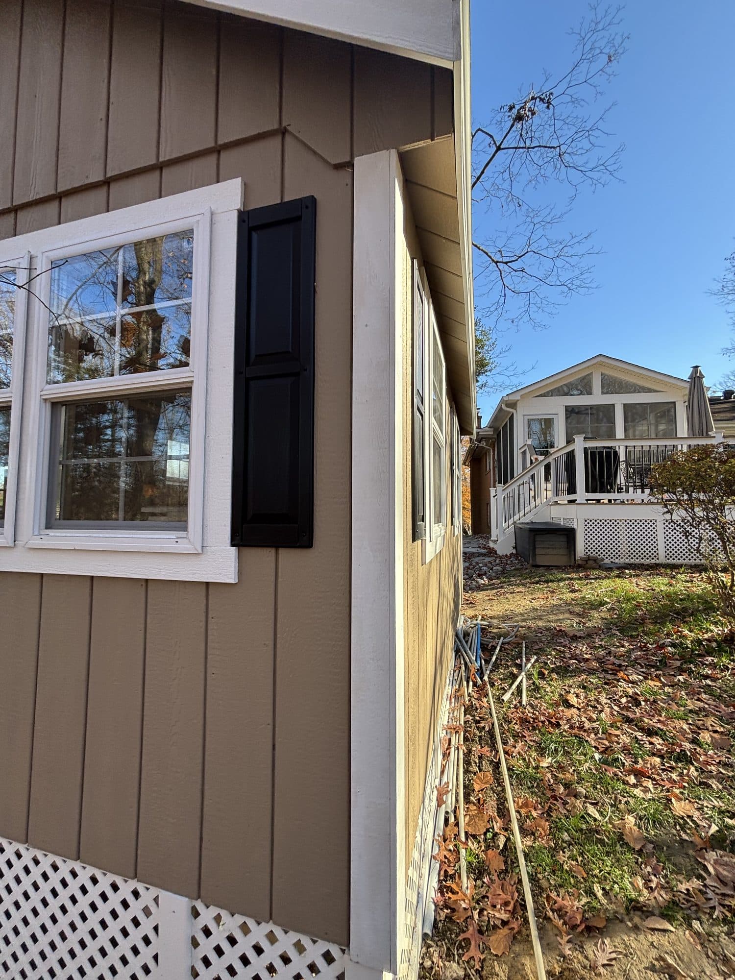 A board-and-batten addition with black-shuttered windows, a sunroom and deck visible beyond. Home addition project by Potts Brothers Construction, Arlington & Northern Virginia