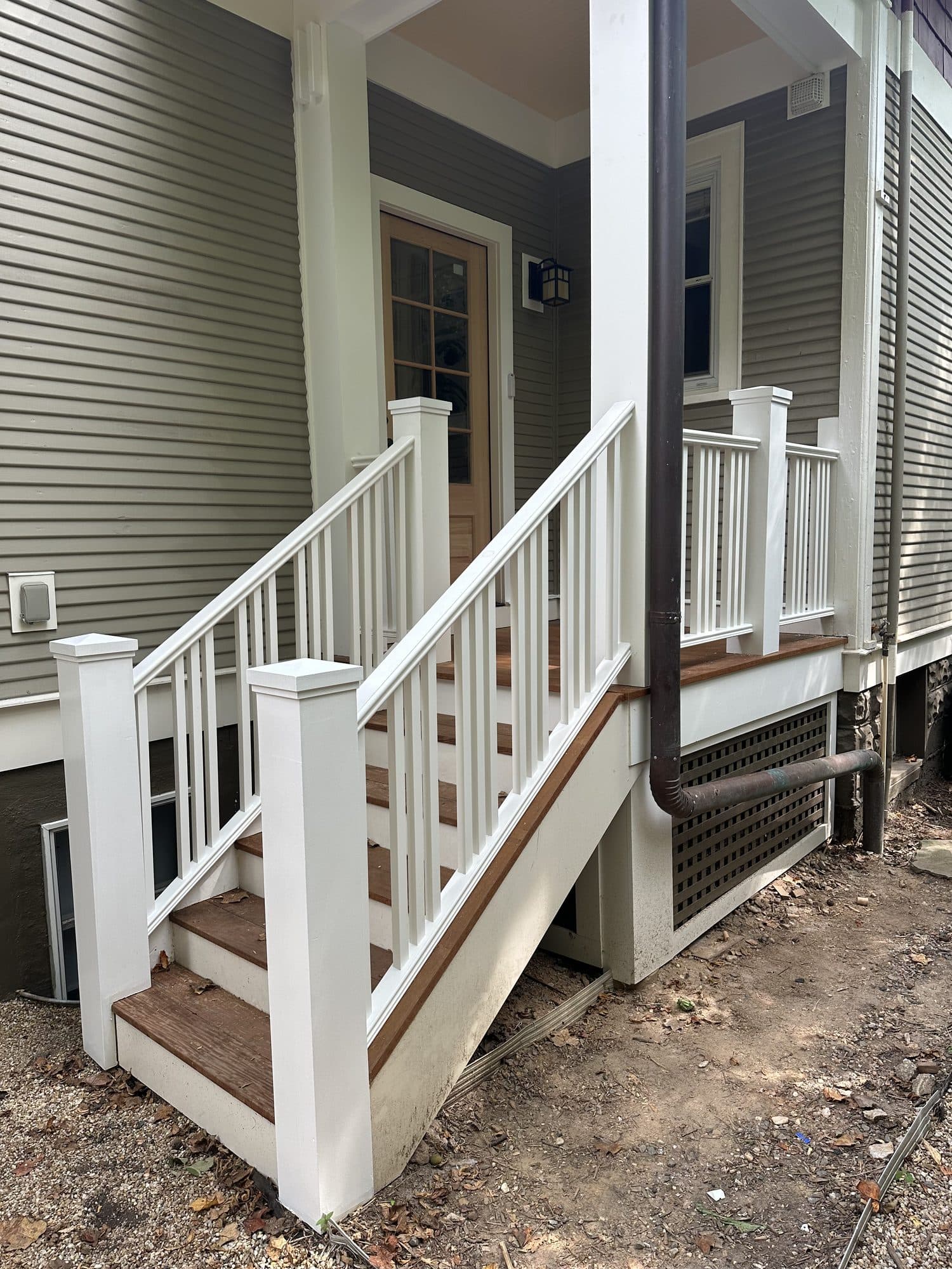 A finished front porch with white turned railings, stained wood treads, and gray lap siding. Home addition project by Potts Brothers Construction, Arlington & Northern Virginia