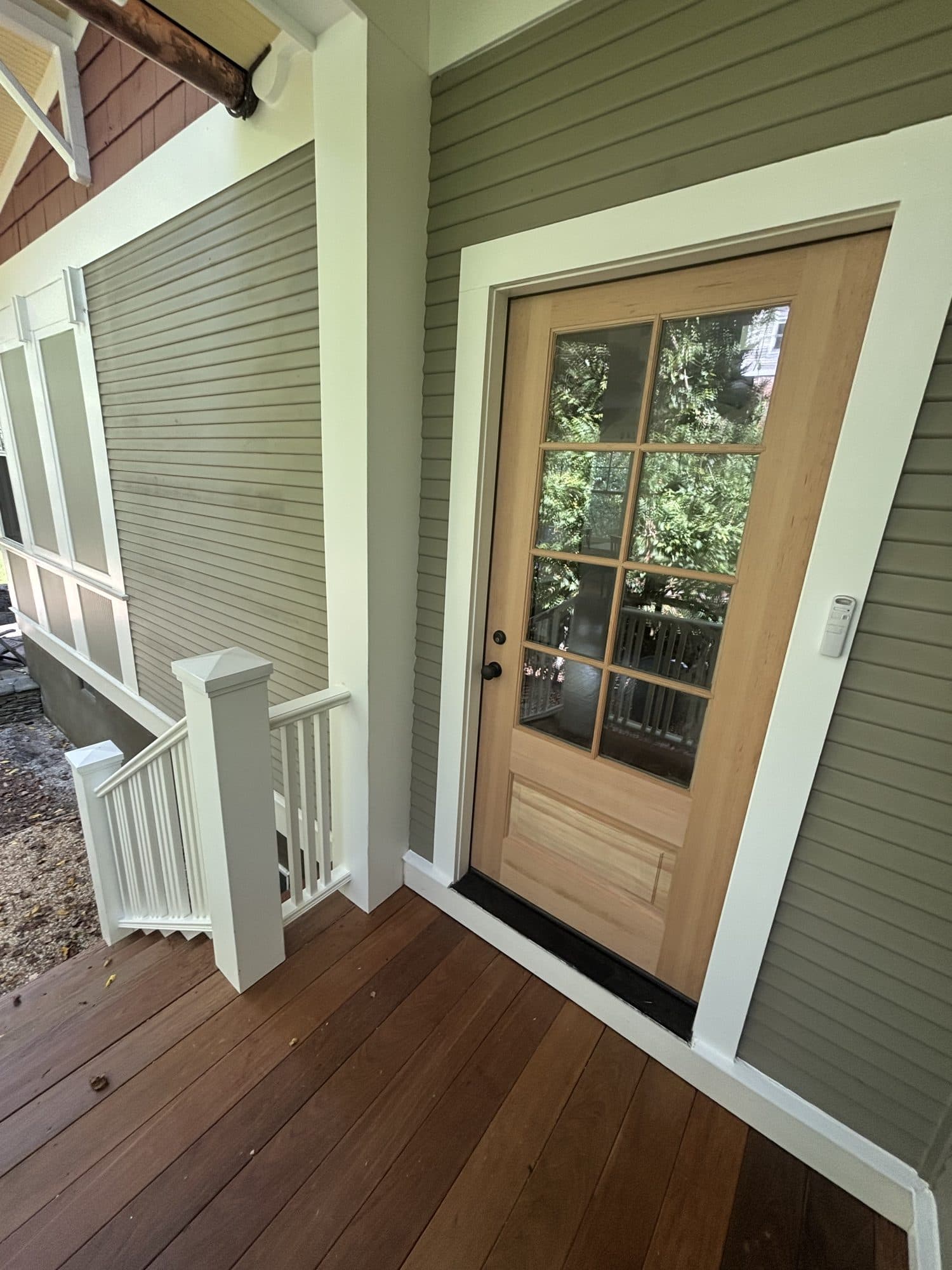 Finished craftsman porch with green siding, white trim, a divided-light wood entry door, and rich hardwood plank decking. Home addition project by Potts Brothers Construction, Arlington & Northern Virginia