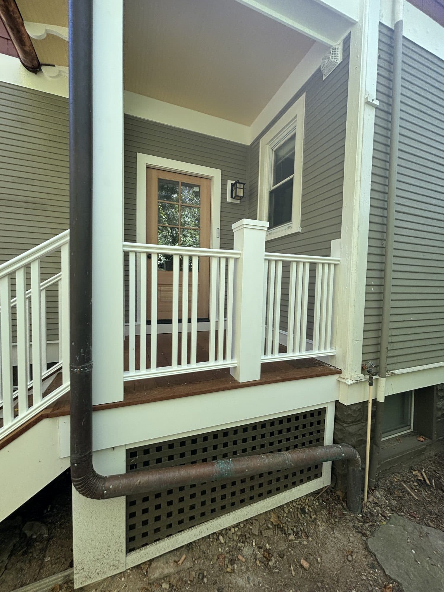 A finished rear porch with white railings, lattice skirting, and a glass-paned door on a craftsman home. Home addition project by Potts Brothers Construction, Arlington & Northern Virginia