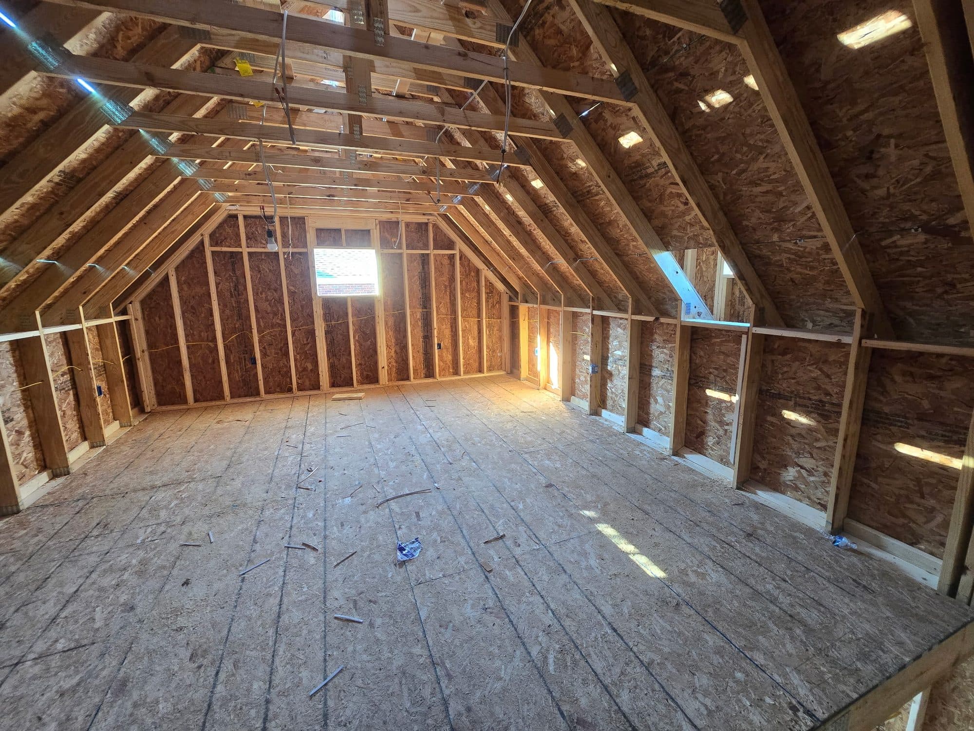 A spacious framed attic conversion with sloped rafters, knee walls, and a new OSB subfloor lit by a dormer. Home addition project by Potts Brothers Construction, Arlington & Northern Virginia