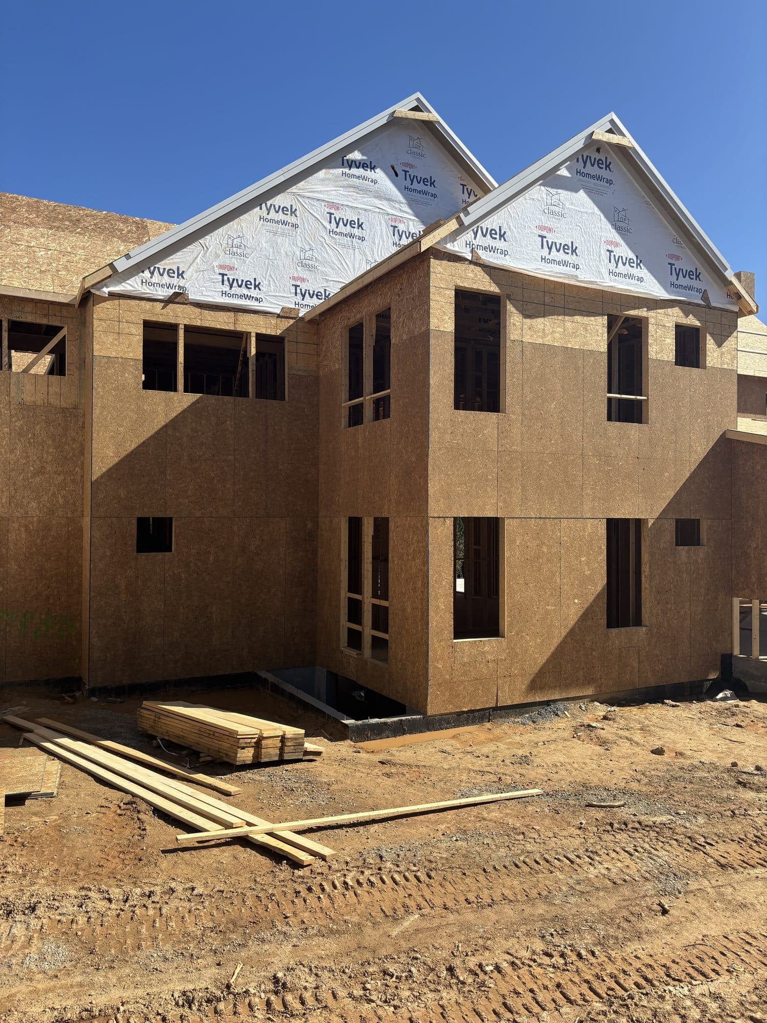A two-story home sheathed in OSB with Tyvek housewrap on the gable ends, awaiting siding. Home addition project by Potts Brothers Construction, Arlington & Northern Virginia