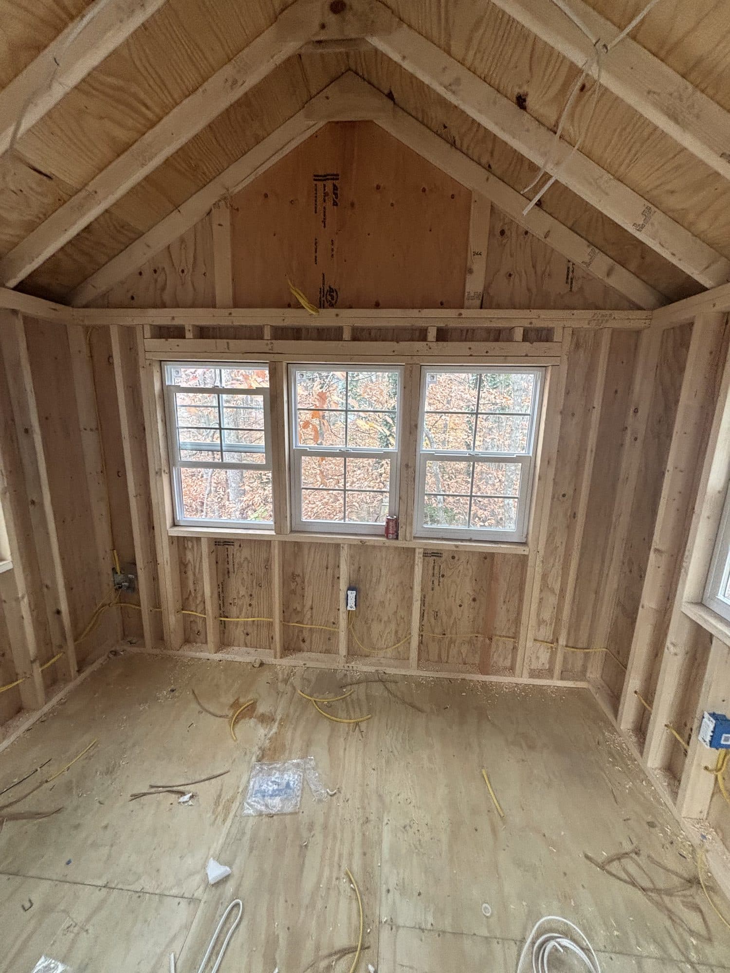 A sunroom addition framed with a vaulted ceiling and a wide bay window looking onto autumn woods. Home addition project by Potts Brothers Construction, Arlington & Northern Virginia
