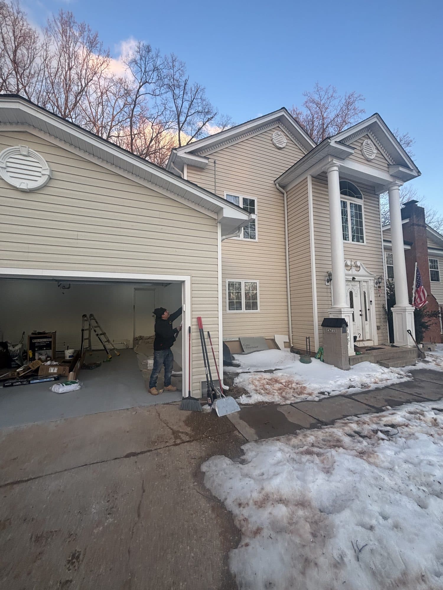 A large two-story home with cream siding, a columned portico entry, and an open attached garage under construction at dusk. Home addition project by Potts Brothers Construction, Arlington & Northern Virginia