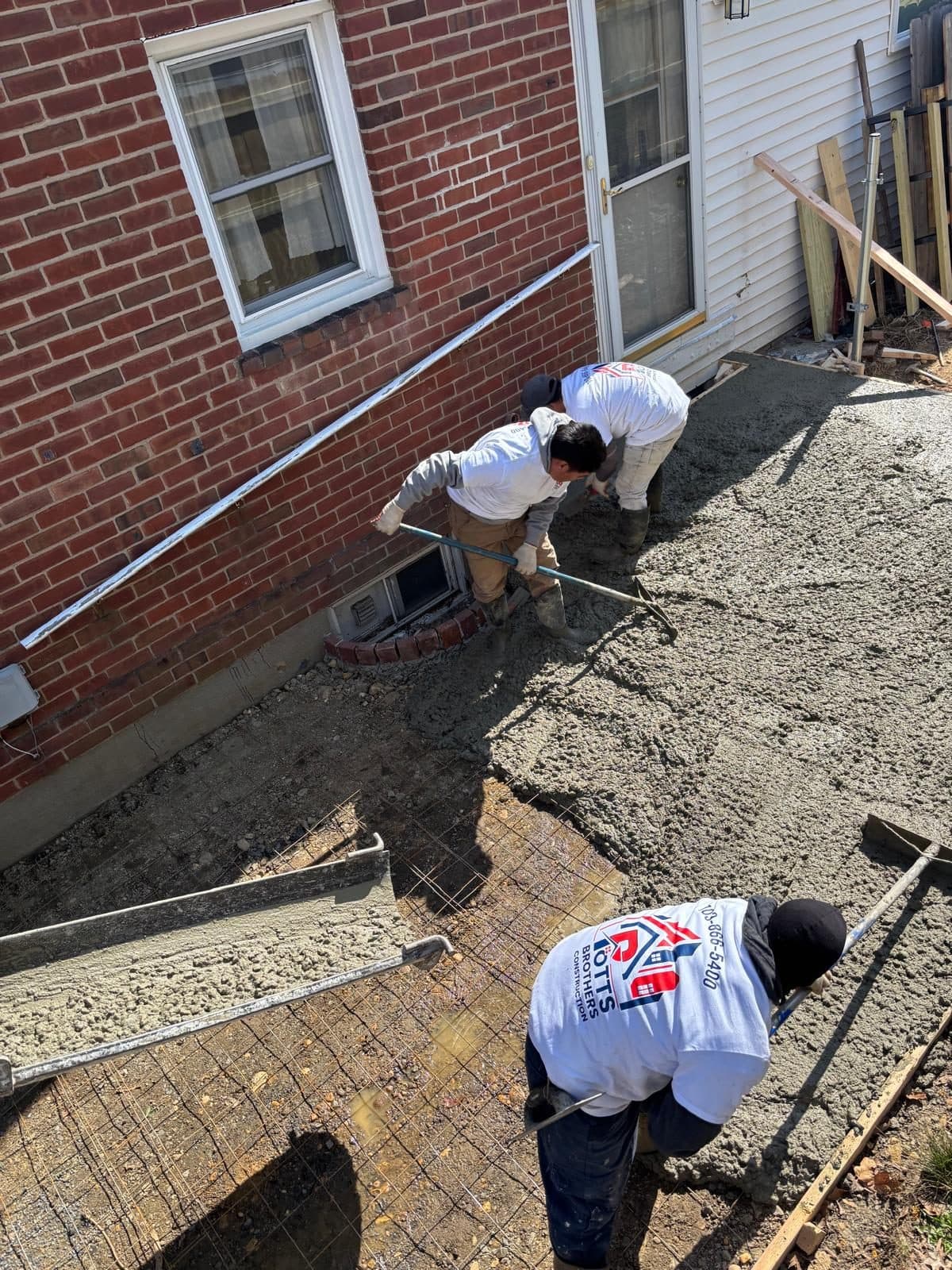 Crew finishing concrete slab over rebar beside brick house. Concrete project by Potts Brothers Construction, Arlington & Northern Virginia