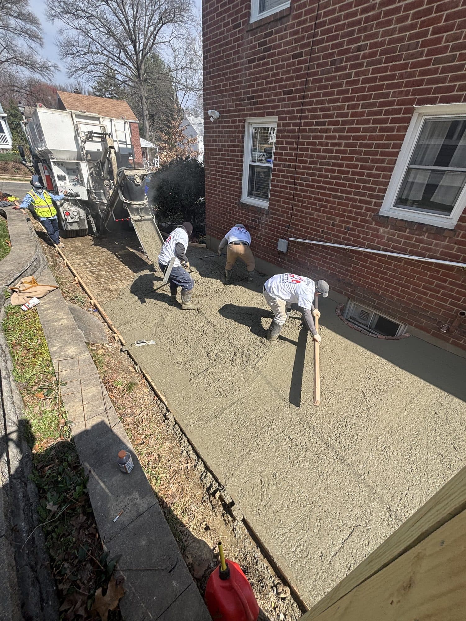 Workers screed and finish a freshly poured concrete walkway running alongside a brick home with a concrete pump truck. Concrete project by Potts Brothers Construction, Arlington & Northern Virginia
