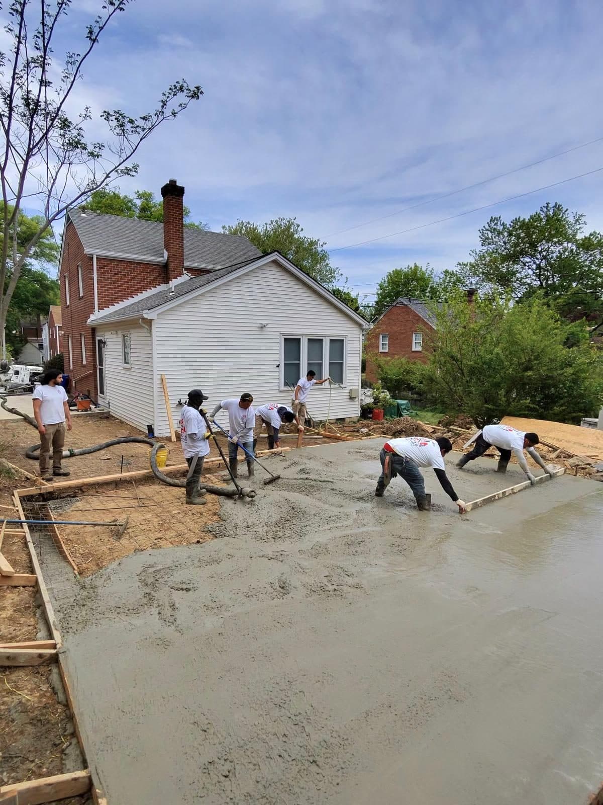Crew pumping and finishing a large freshly poured concrete slab behind a home. Concrete project by Potts Brothers Construction, Arlington & Northern Virginia
