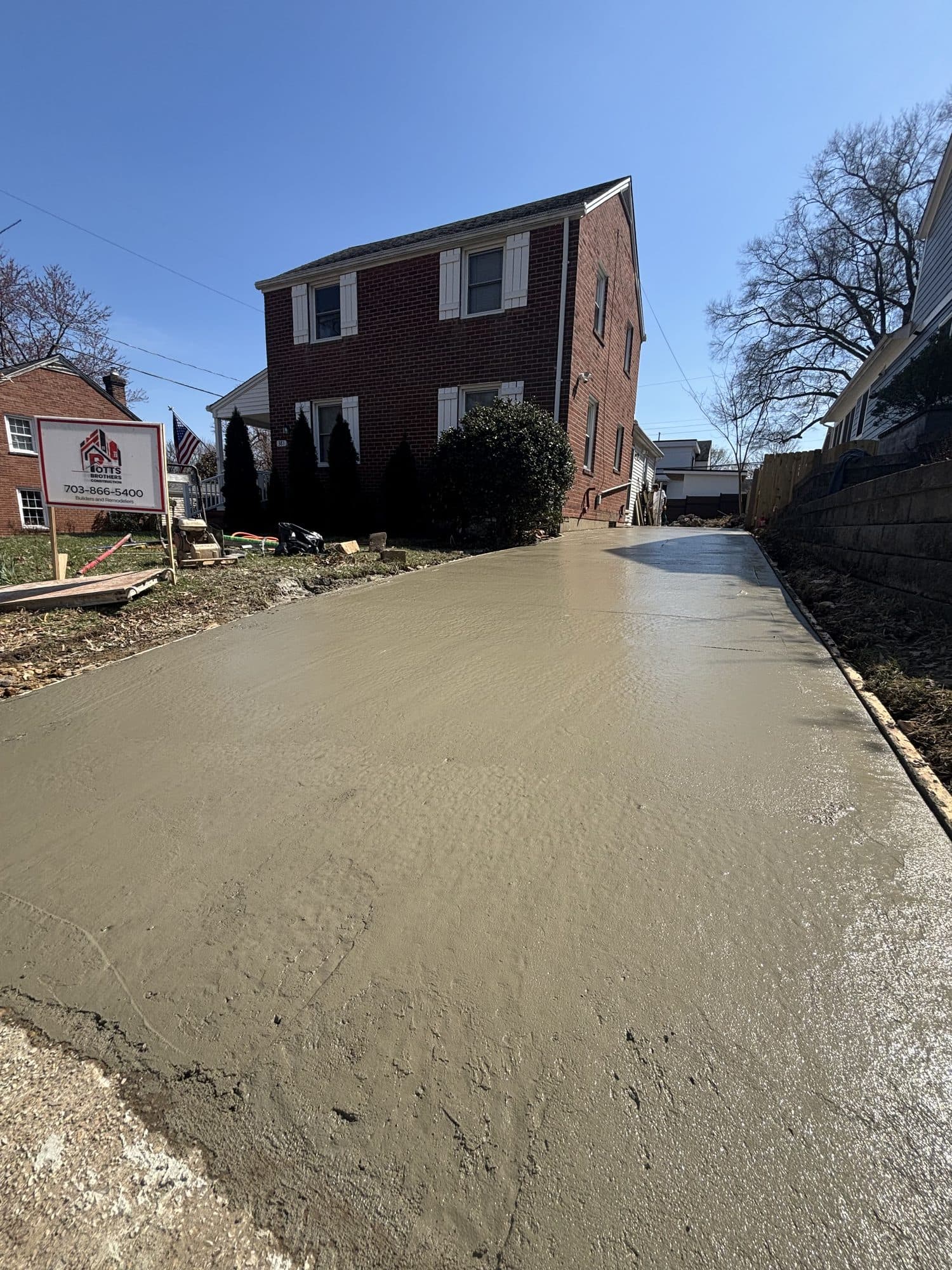 A wide freshly finished concrete driveway extends toward a two-story brick home under a clear blue sky. Concrete project by Potts Brothers Construction, Arlington & Northern Virginia