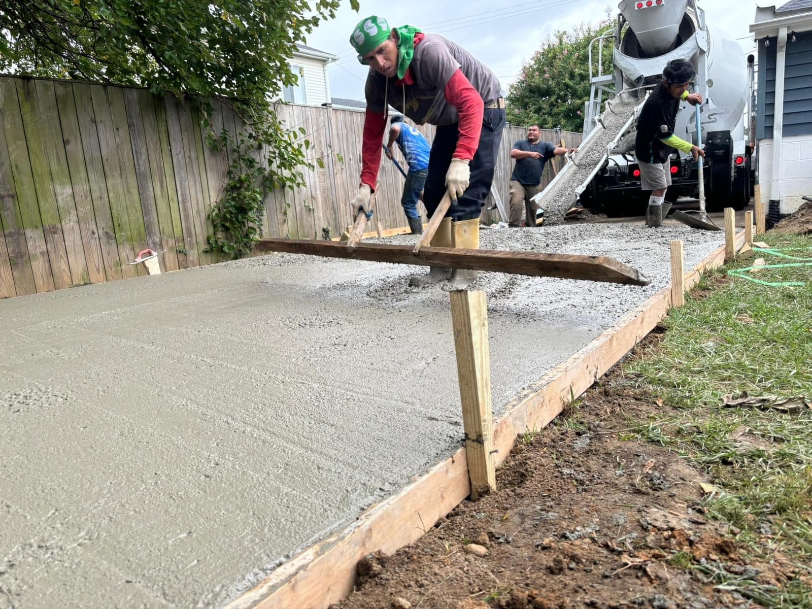 Worker screeding a freshly poured concrete walkway set in formed edges beside a fence. Concrete project by Potts Brothers Construction, Arlington & Northern Virginia