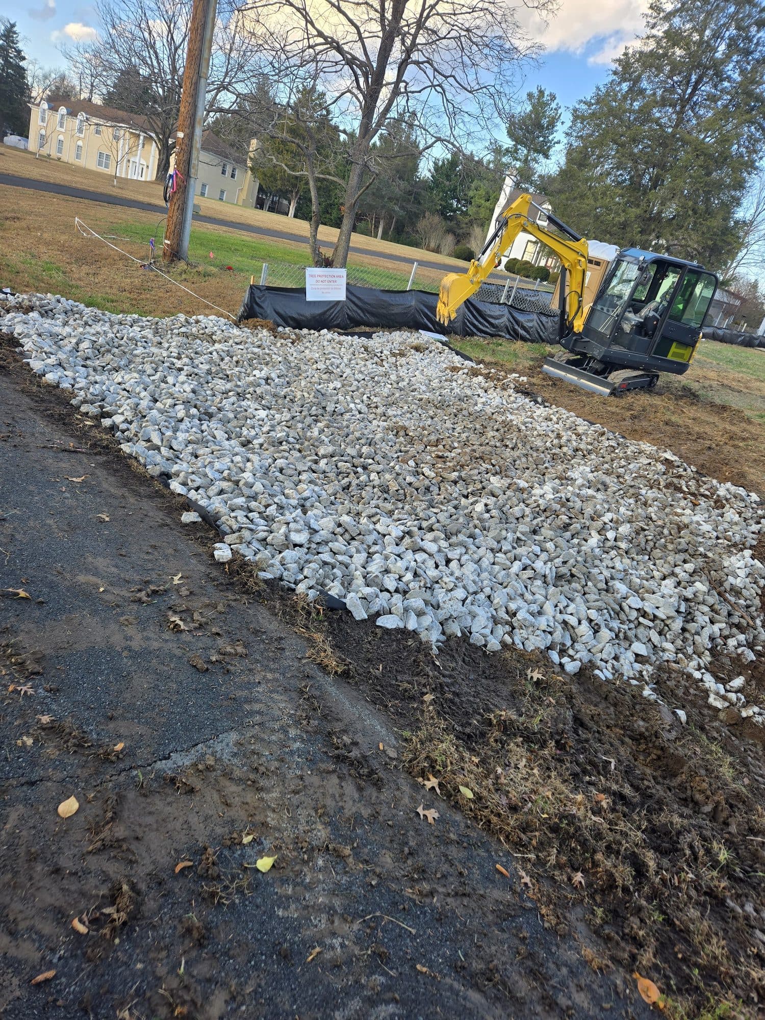 Freshly placed crushed-stone drainage bed with silt fencing and a mini-excavator on site. Foundation project by Potts Brothers Construction, Arlington & Northern Virginia