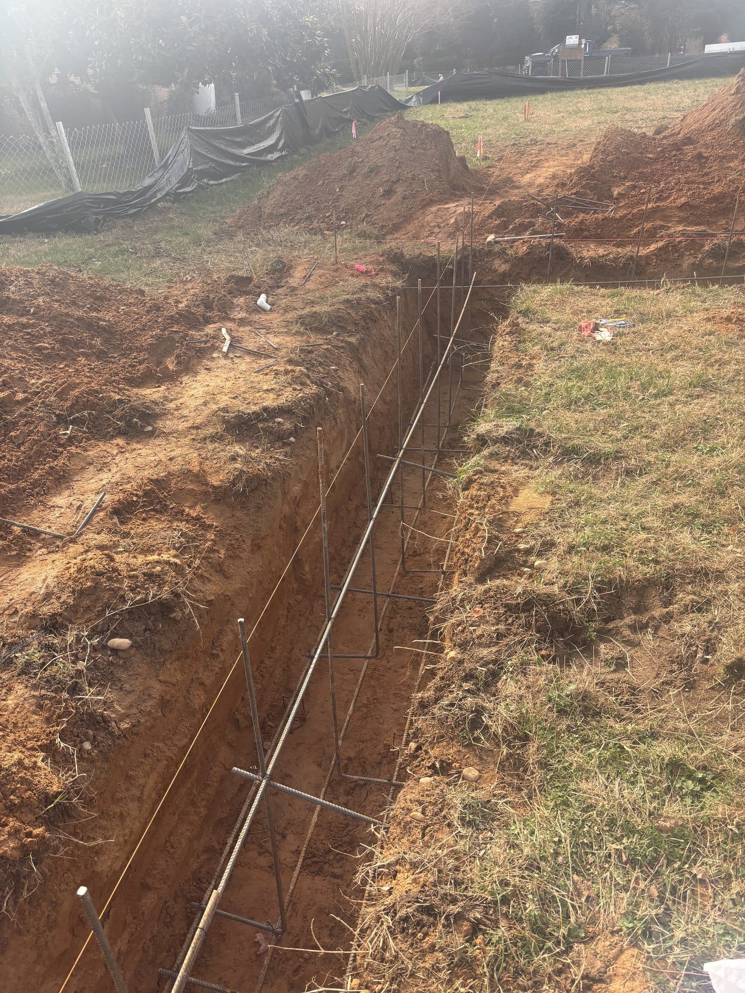 A foundation footing trench fitted with a continuous steel rebar cage in red clay soil. Foundation project by Potts Brothers Construction, Arlington & Northern Virginia
