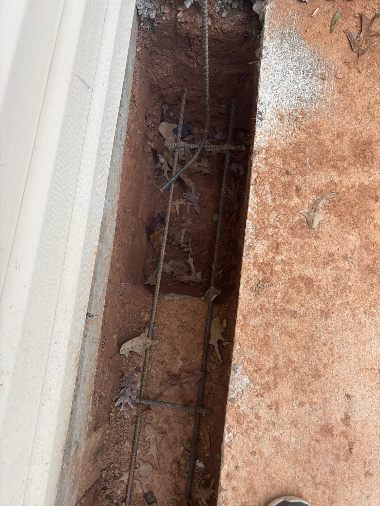 Foundation footing trench with horizontal and vertical rebar reinforcement against an existing wall. Foundation project by Potts Brothers Construction, Arlington & Northern Virginia
