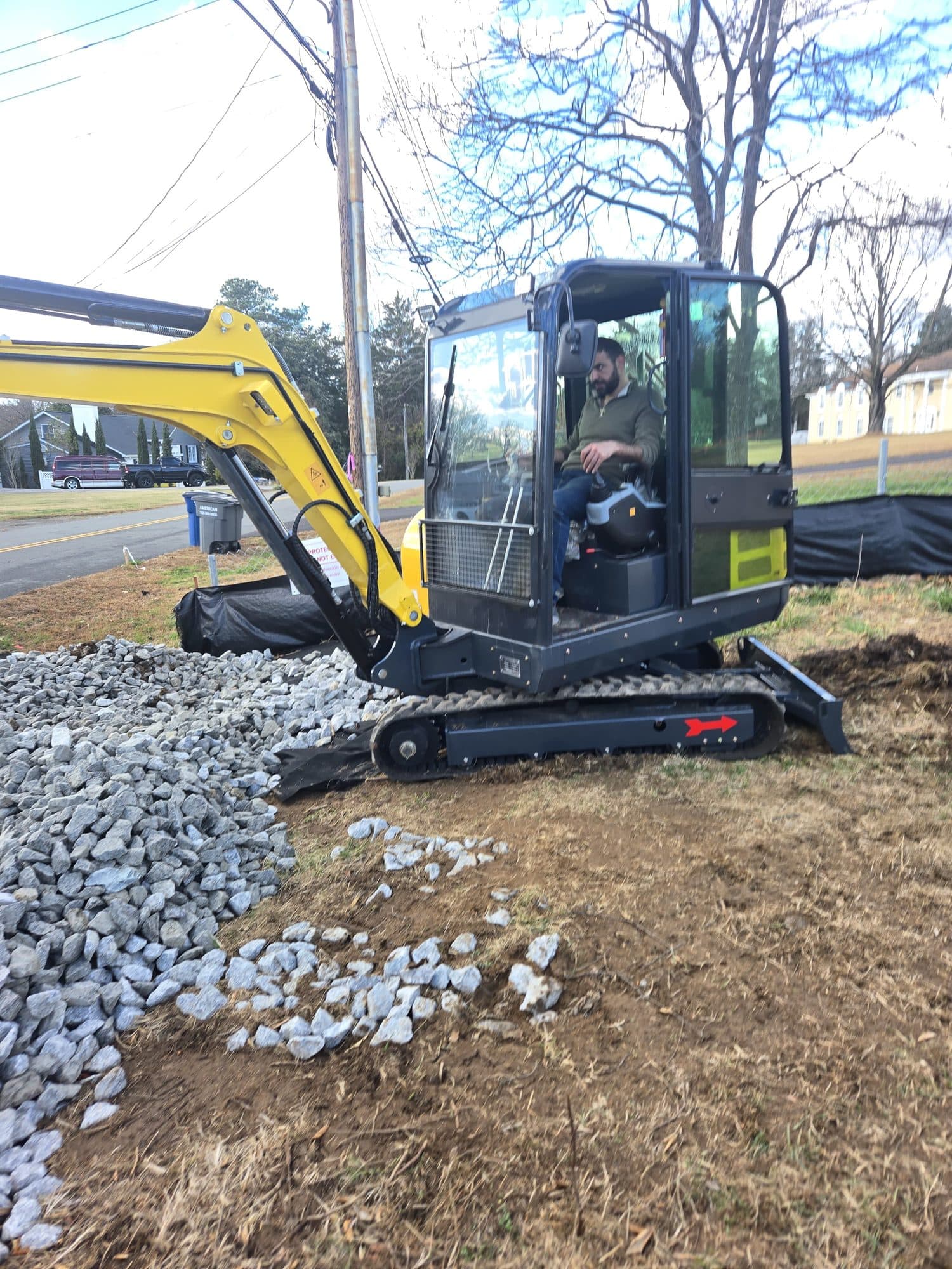 Operator using a mini-excavator to spread crushed stone for a drainage and foundation base. Foundation project by Potts Brothers Construction, Arlington & Northern Virginia