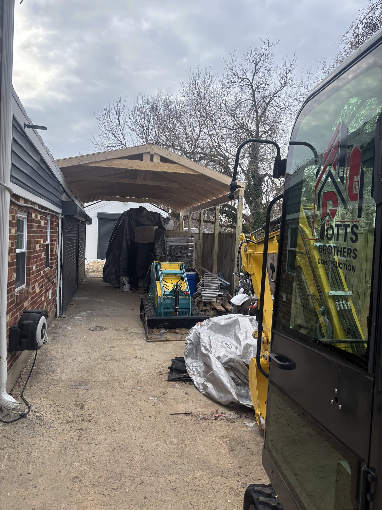 A timber-framed garage gable rises beside a brick home as a Potts Brothers Construction van is parked in the work area. Garage project by Potts Brothers Construction, Arlington & Northern Virginia