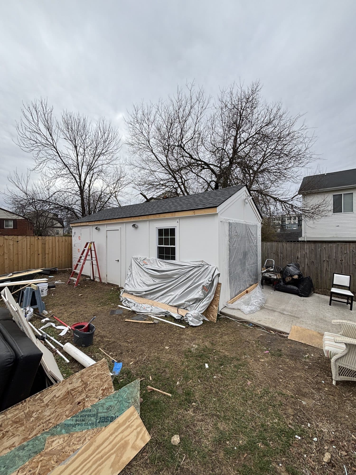 A white detached garage-shed with new shingles nearing completion in a fenced backyard. Garage project by Potts Brothers Construction, Arlington & Northern Virginia