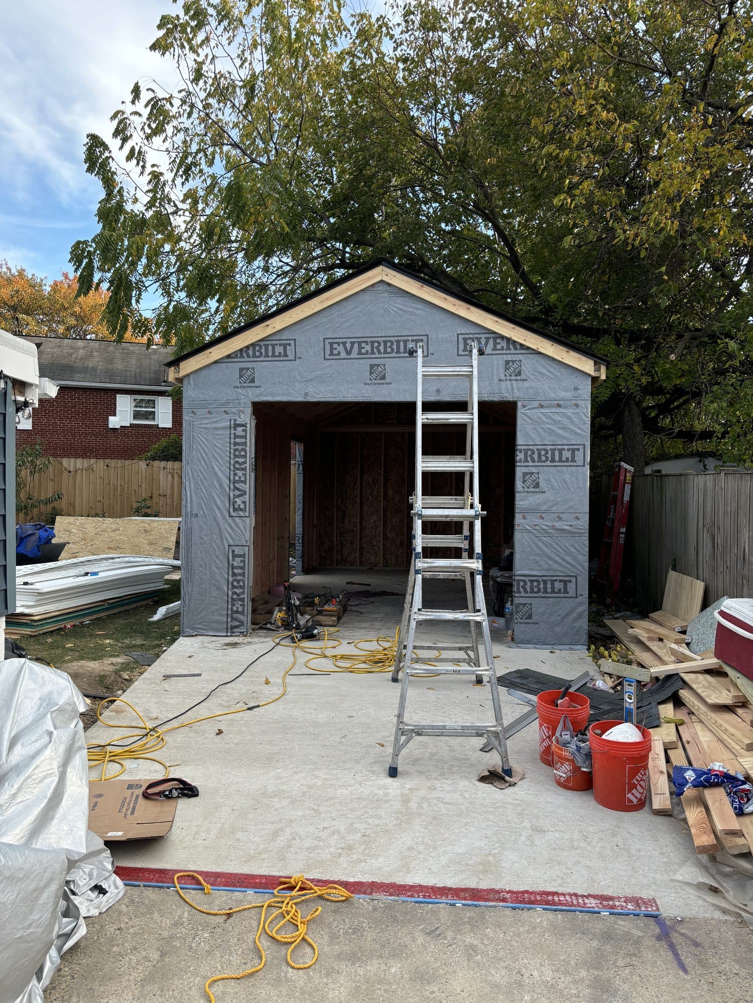 A detached garage wrapped in house wrap with its open bay and a ladder set inside on the fresh concrete slab. Garage project by Potts Brothers Construction, Arlington & Northern Virginia