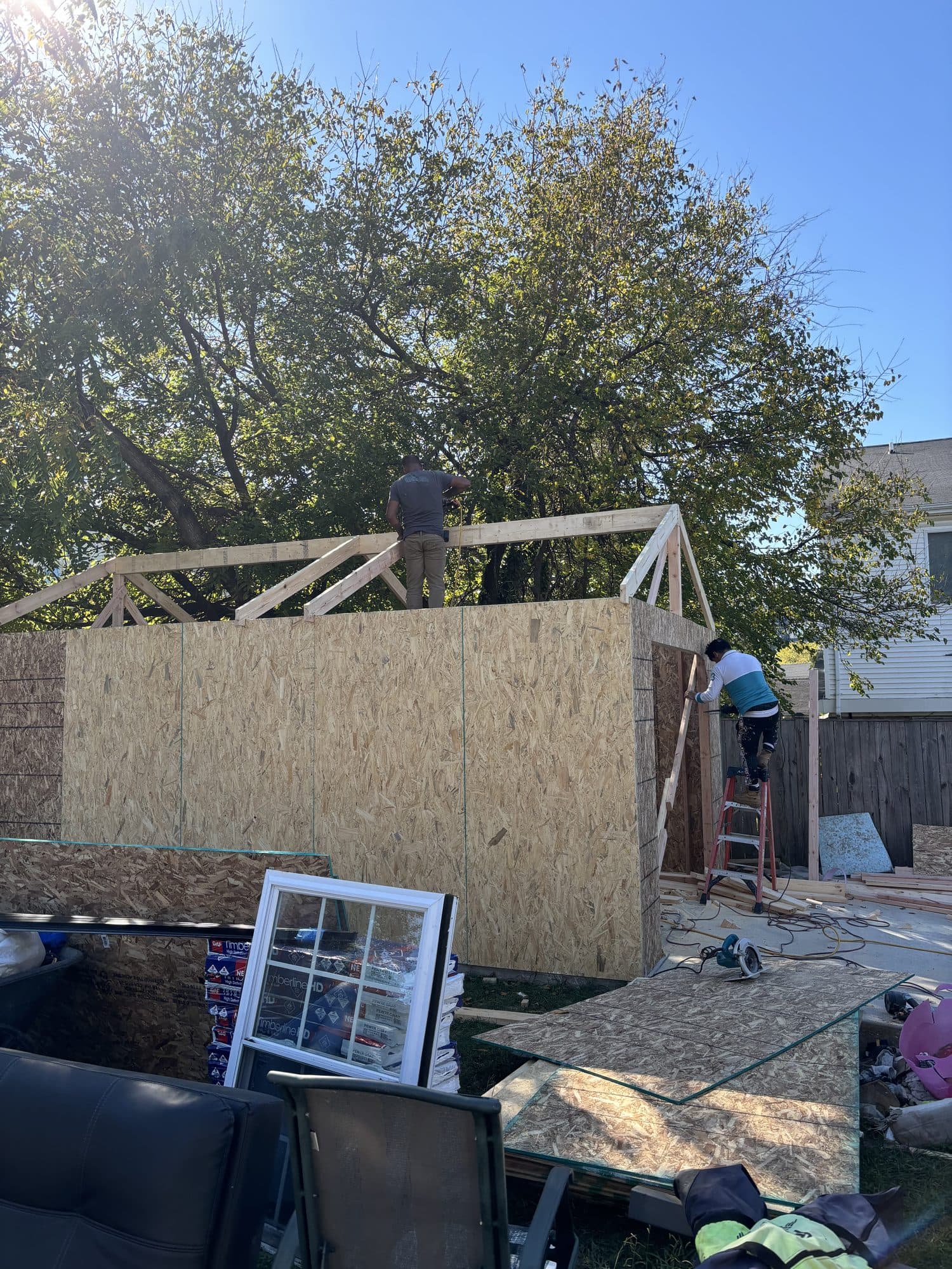 Two crew members frame the rafters atop an OSB-sheathed detached garage-shed in a backyard. Garage project by Potts Brothers Construction, Arlington & Northern Virginia