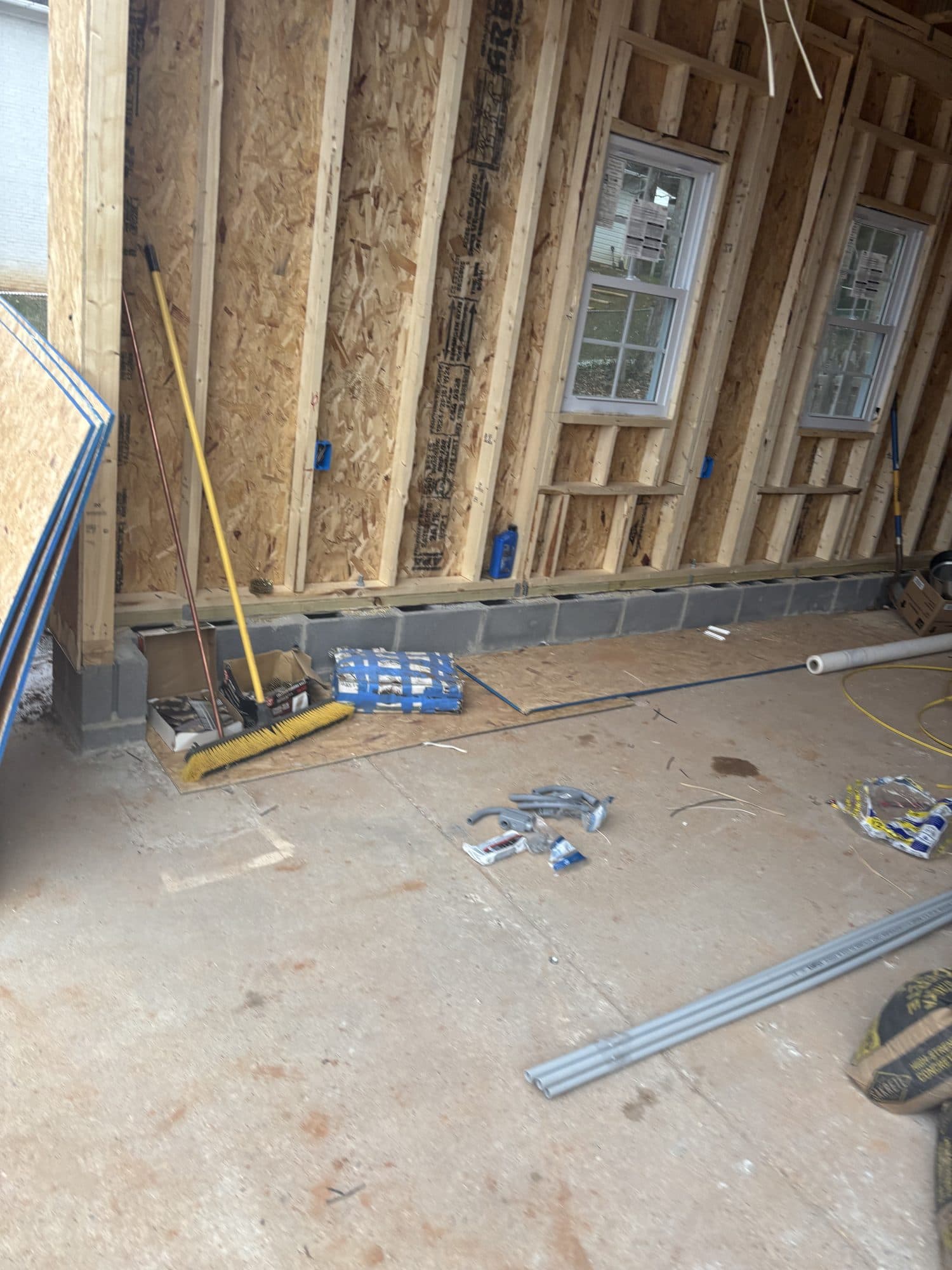 Interior of a detached garage under construction with OSB-sheathed stud walls, new vinyl windows, and a block foundation curb. Garage project by Potts Brothers Construction, Arlington & Northern Virginia