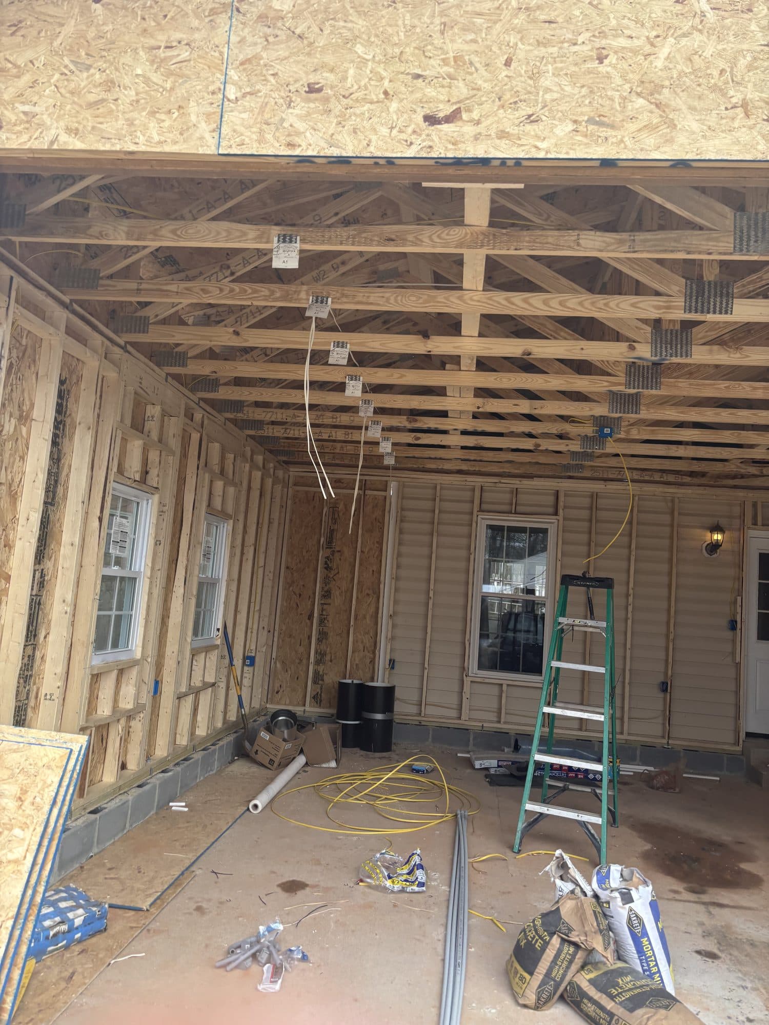 Interior of a framed garage with OSB walls, exposed ceiling joists, a green ladder, and tools on the concrete floor. Garage project by Potts Brothers Construction, Arlington & Northern Virginia