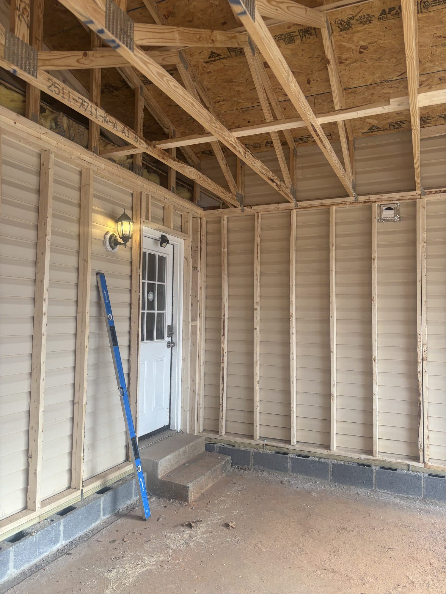 Inside a framed garage with vinyl-clad walls, a white side entry door, exposed trusses, and a concrete floor. Garage project by Potts Brothers Construction, Arlington & Northern Virginia