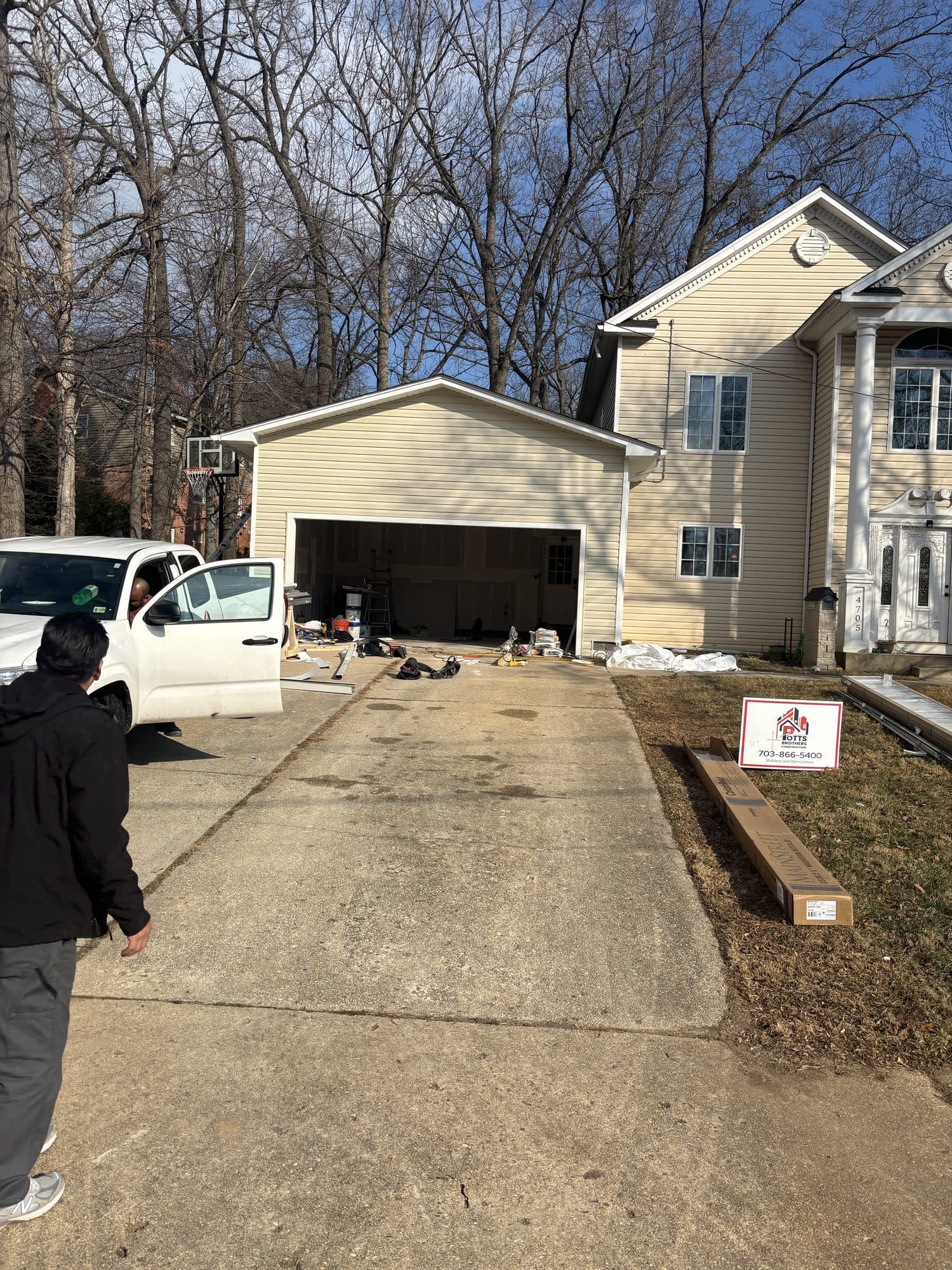 A finished attached two-car garage with tan siding at the end of a long driveway, with a Potts Brothers yard sign in the lawn. Garage project by Potts Brothers Construction, Arlington & Northern Virginia