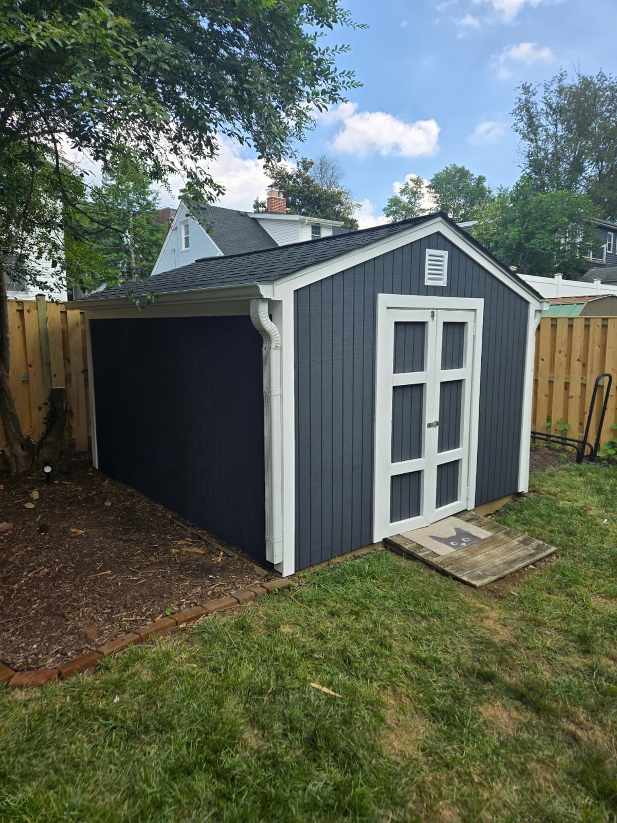 A finished detached garage with dark gray siding, a shingled gable, white corner trim, and an open garage bay beside a side entry door. Garage project by Potts Brothers Construction, Arlington & Northern Virginia