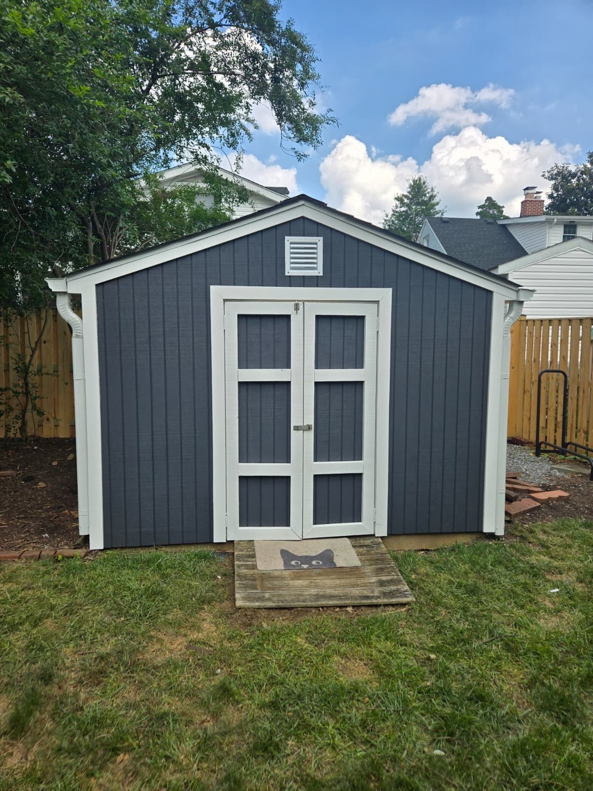 A newly built detached backyard structure with dark gray board-and-batten siding, crisp white trim, and double doors set on a fenced lawn. Garage project by Potts Brothers Construction, Arlington & Northern Virginia