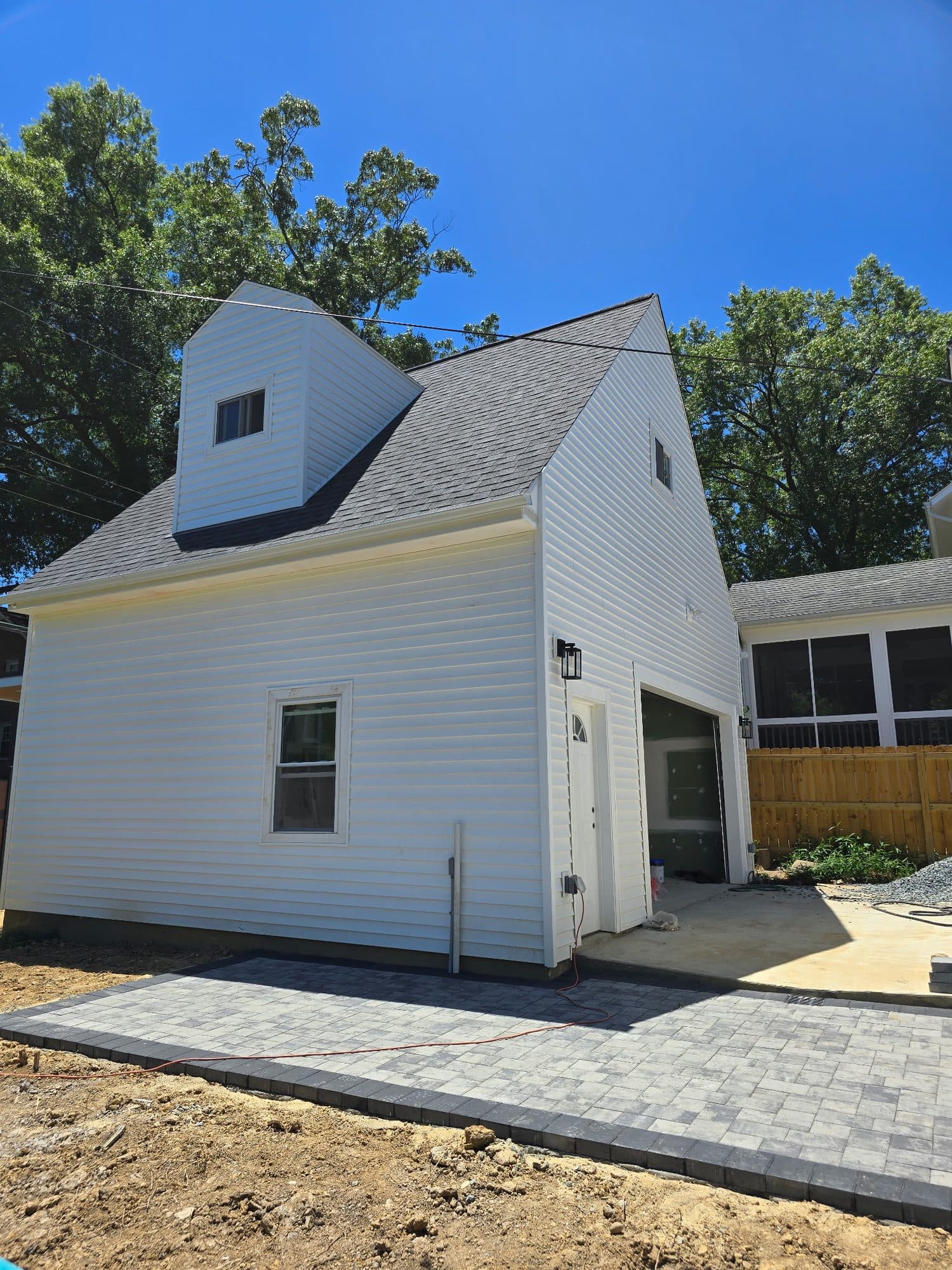 A finished two-story detached garage with white siding, a dormer, shingled gable, and a fresh paver apron at the bay opening. Garage project by Potts Brothers Construction, Arlington & Northern Virginia