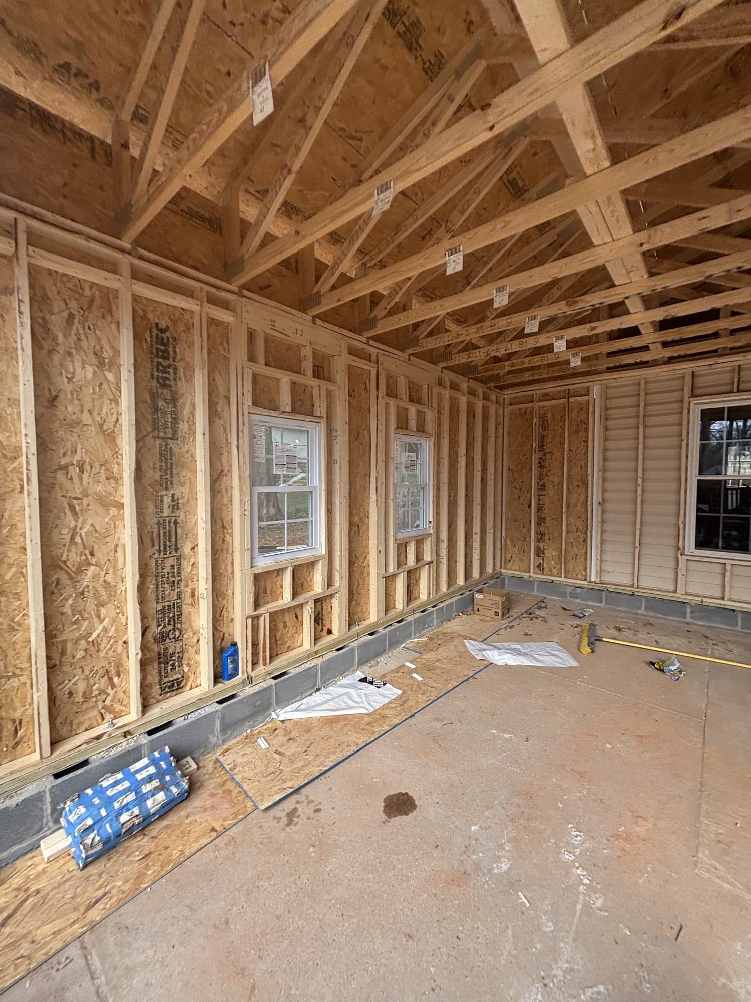Interior of a newly framed detached garage with rafter trusses, OSB-sheathed walls, and several installed windows. Garage project by Potts Brothers Construction, Arlington & Northern Virginia
