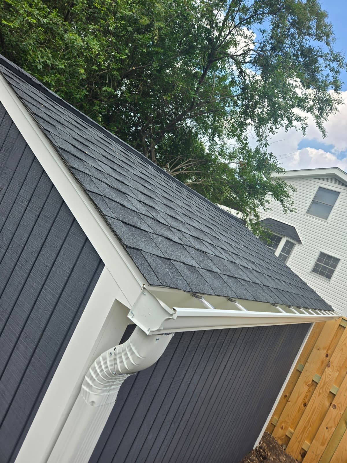 Eave and gable detail of a detached garage with new charcoal shingles, white fascia, and a freshly installed gutter and downspout. Garage project by Potts Brothers Construction, Arlington & Northern Virginia